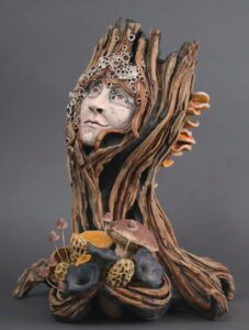 Ceramic sculpture depicting a tree trunk with a woman's head with a bouquet of mushrooms.